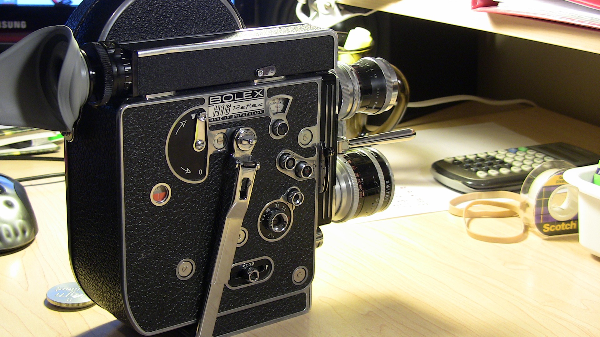 Image of this image features a vintage bolex h16 reflex camera, renowned for its use in professional filmmaking. the 16mm film camera is displayed on a wooden office desk alongside a calculator and stationery, highlighting its classic design and mechanical dials. ideal