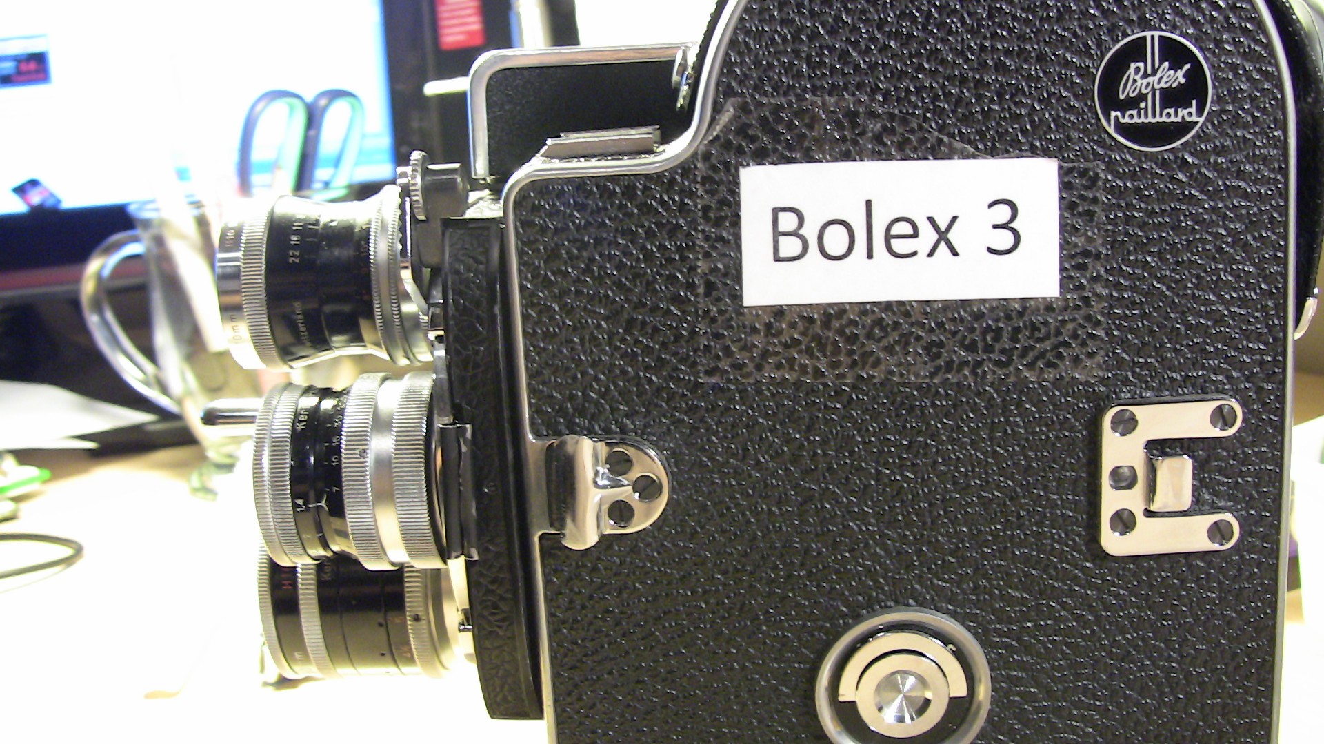Image of the image features a vintage bolex 3, a classic 16mm film camera renowned for its durability and precision in filmmaking. the camera is showcased on a desk, highlighting its textured black body and multiple lenses, offering a glimpse into retro cinemat