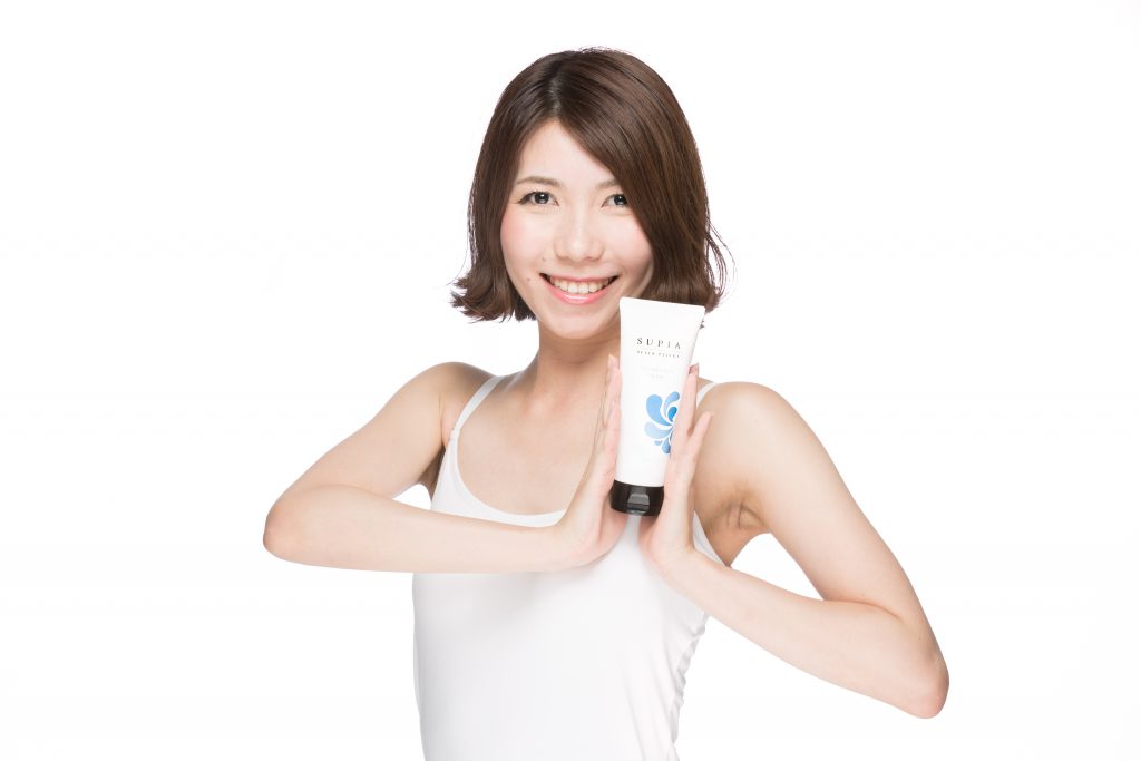 Image of a smiling woman holding a skincare product tube against a white background. she wears a white tank top and showcases the product with confidence. ideal for content focusing on beauty, skincare, and personal care products.