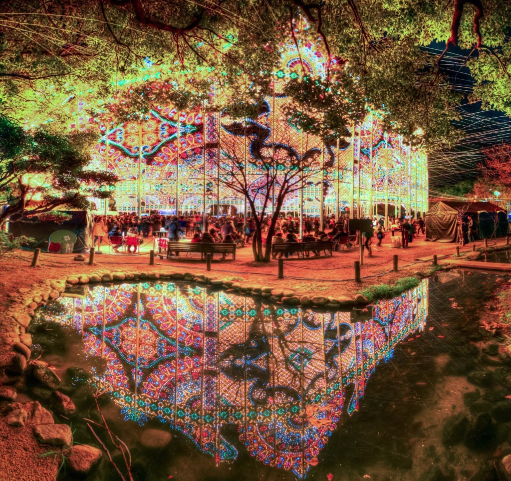 Image of this captivating image showcases a vibrant light festival in a serene park setting, featuring intricate, colorful illuminations reflecting beautifully on a tranquil pond. the scene, set against a backdrop of lush trees, depicts a lively gathering of people enjoying the mesmerizing display. perfect