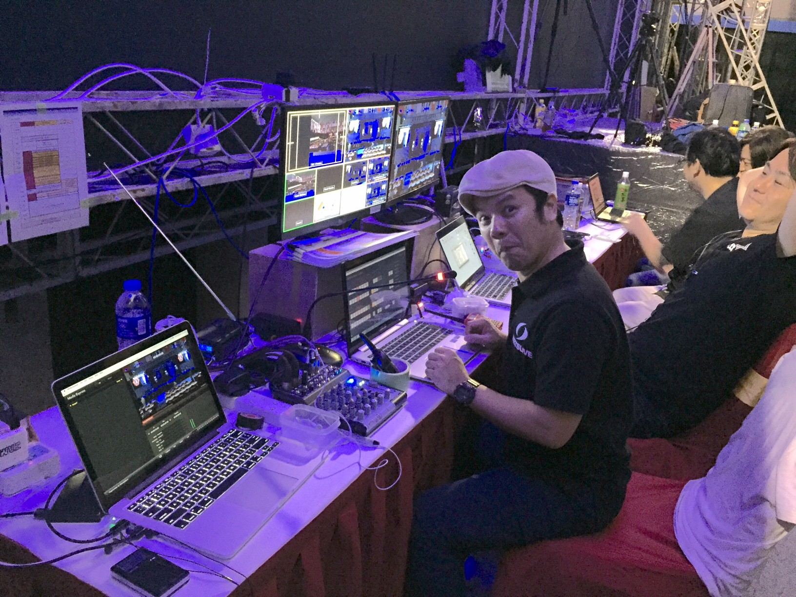 Image of backstage production control room featuring crew members managing live event broadcasting. the setup includes multiple monitors, laptops, and audio equipment, highlighting a dynamic workspace in media production. ideal location for event management, live streaming, and technical coordination.