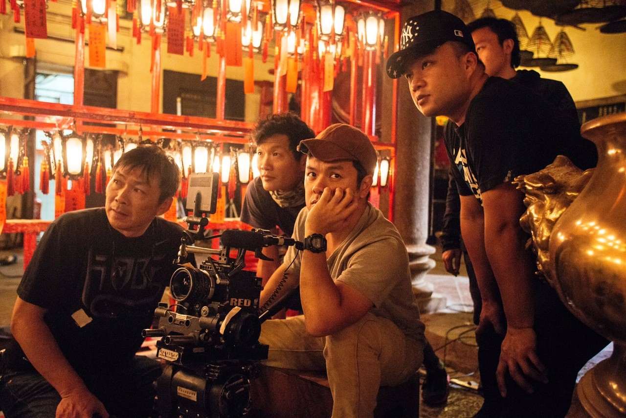 Image of behind-the-scenes image featuring a film crew analyzing a scene inside an asian temple. the intricate decor includes vibrant red lanterns, providing a unique cinematic atmosphere. the crew is focused around a professional camera setup, discussing lighting and angles, highlighting the collaborative nature