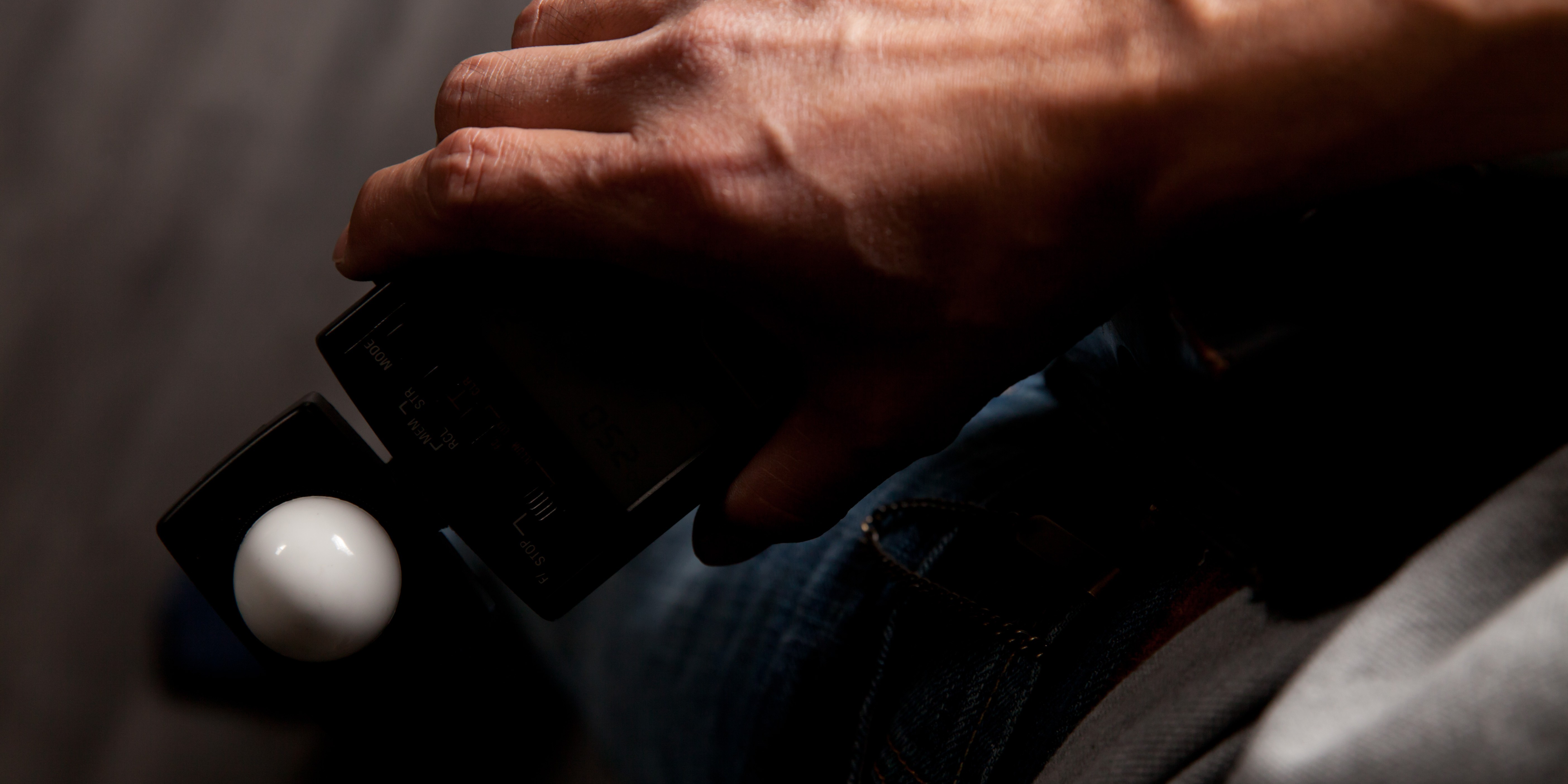 Image of close-up photo of a hand holding a light meter, commonly used in photography to measure exposure. the device is positioned over a dark background, emphasizing its design and functionality. this image is ideal for content related to photography equipment, light measurement, and camera
