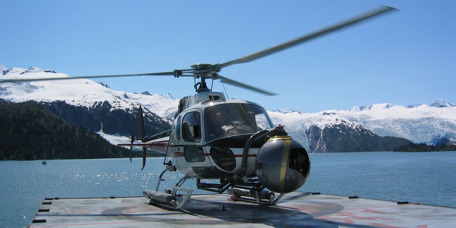 Image of a helicopter is poised on a landing pad beside a breathtaking glacial landscape, set against snow-covered mountains under a clear blue sky. this dramatic scene captures the essence of adventure and exploration, perfect for travel enthusiasts and nature lovers seeking unique aerial experiences in remote