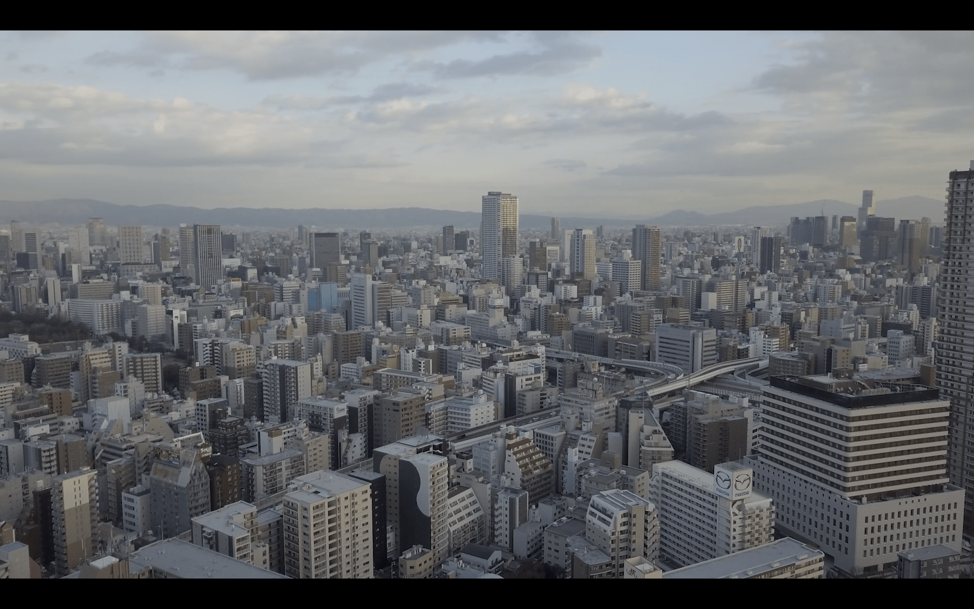 Image of aerial view of a sprawling cityscape in osaka, japan, featuring numerous high-rise buildings and skyscrapers under a partly cloudy sky. the urban landscape showcases modern architecture and busy infrastructure, highlighting osaka's dynamic metropolis. the image captures the city's expansive skyline