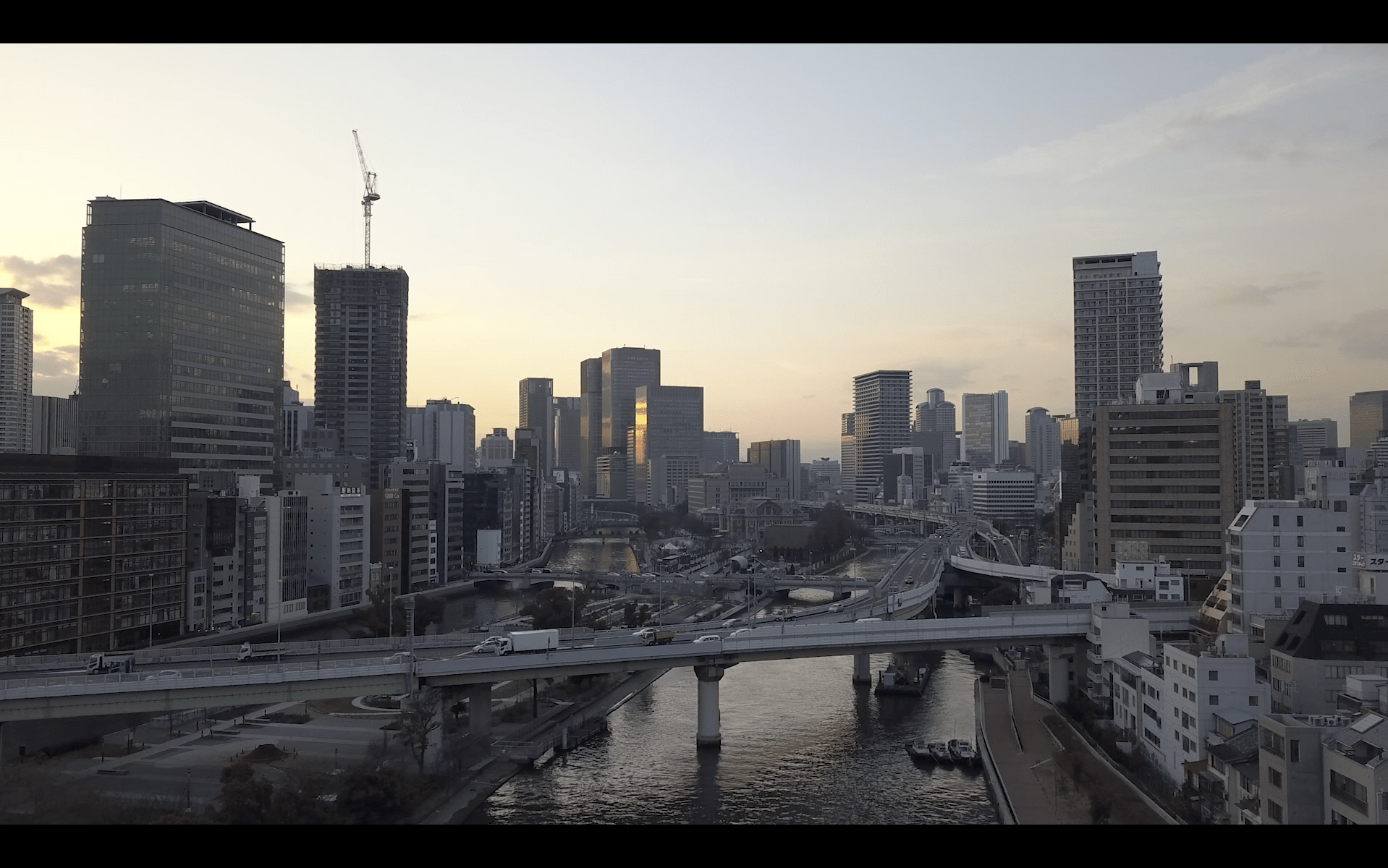 Image of this image showcases a stunning aerial view of a modern urban skyline in osaka, japan, during sunset. highlighting skyscrapers reflecting golden hues, it captures the bustling city life with highways and rivers interwoven throughout the metropolitan landscape. the serene twilight adds a