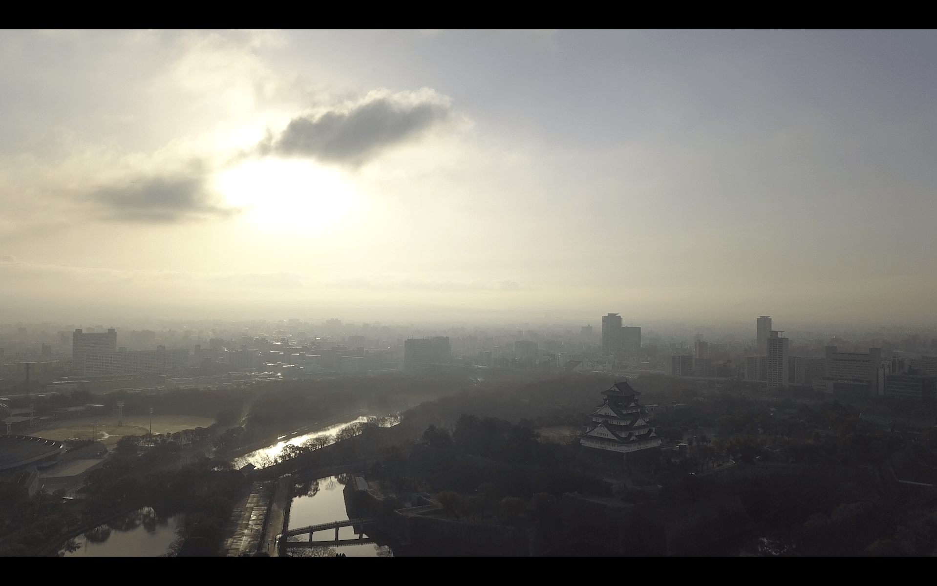 Image of aerial view of osaka castle bathed in the serene light of dawn, with the cityscape of osaka, japan stretching into the horizon. the sky is overcast, creating a mystical atmosphere over this historic landmark and its surrounding urban landscape. perfect for