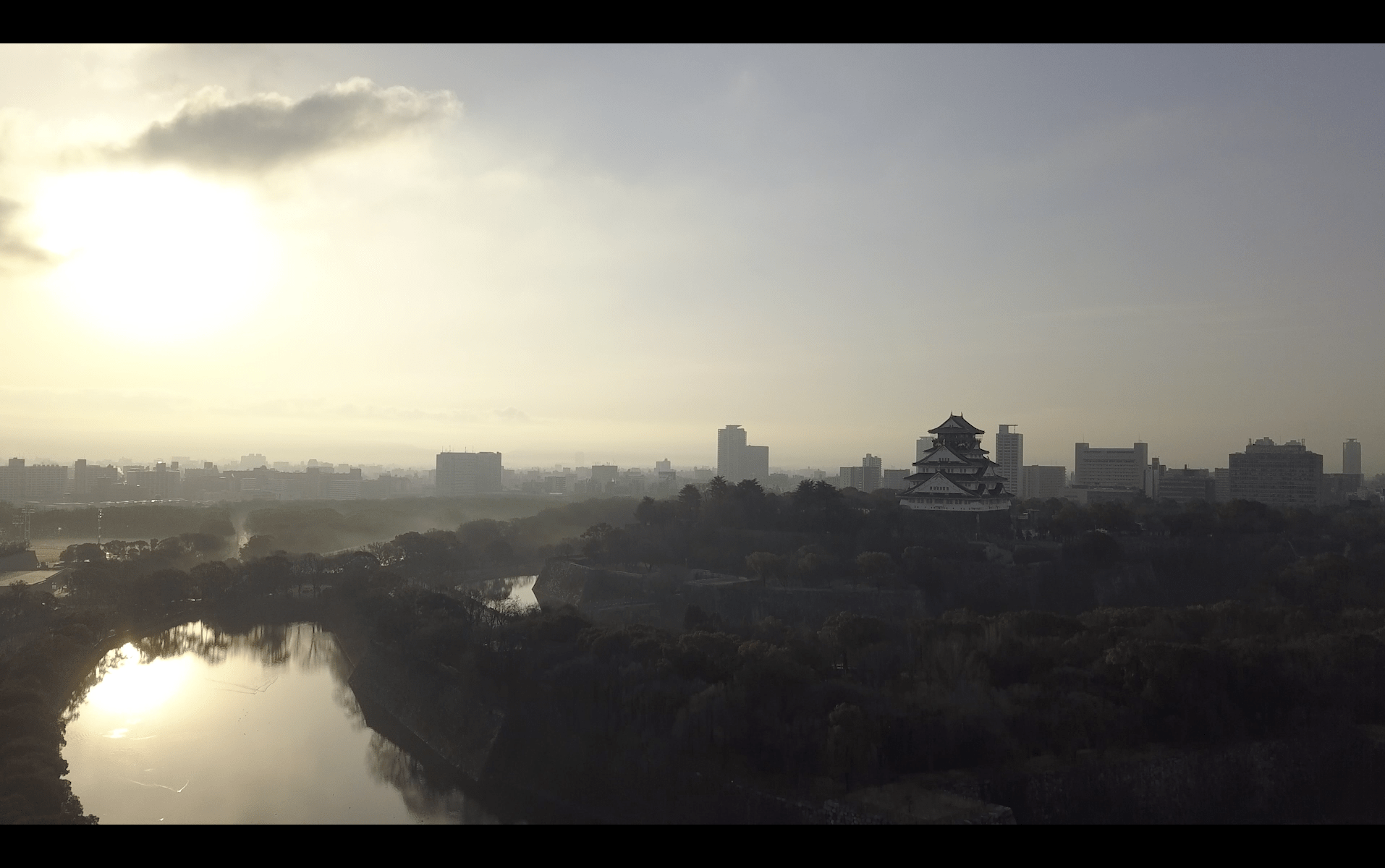Image of this image captures a breathtaking view of osaka castle in japan at sunrise. the iconic castle stands majestically against the city's skyline, surrounded by lush greenery and a serene moat reflecting the early morning light. the golden hues of the dawn create a tranquil atmosphere,