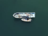 Image of aerial view of a large fishing boat moored alongside a smaller vessel in calm, deep green waters. this nautical scene captures marine life and boating activities, highlighting themes of fishing, ocean travel, and maritime lifestyle. perfect for content related to boating,