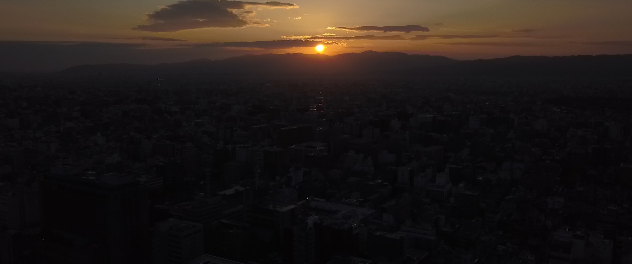 Image of sunset over a sprawling cityscape, with the vibrant orange and yellow hues illuminating the sky above silhouetted urban buildings. mountain ranges border the horizon, adding depth to the breathtaking view. perfect scene for themes of urban sunset, city skyline, and nature