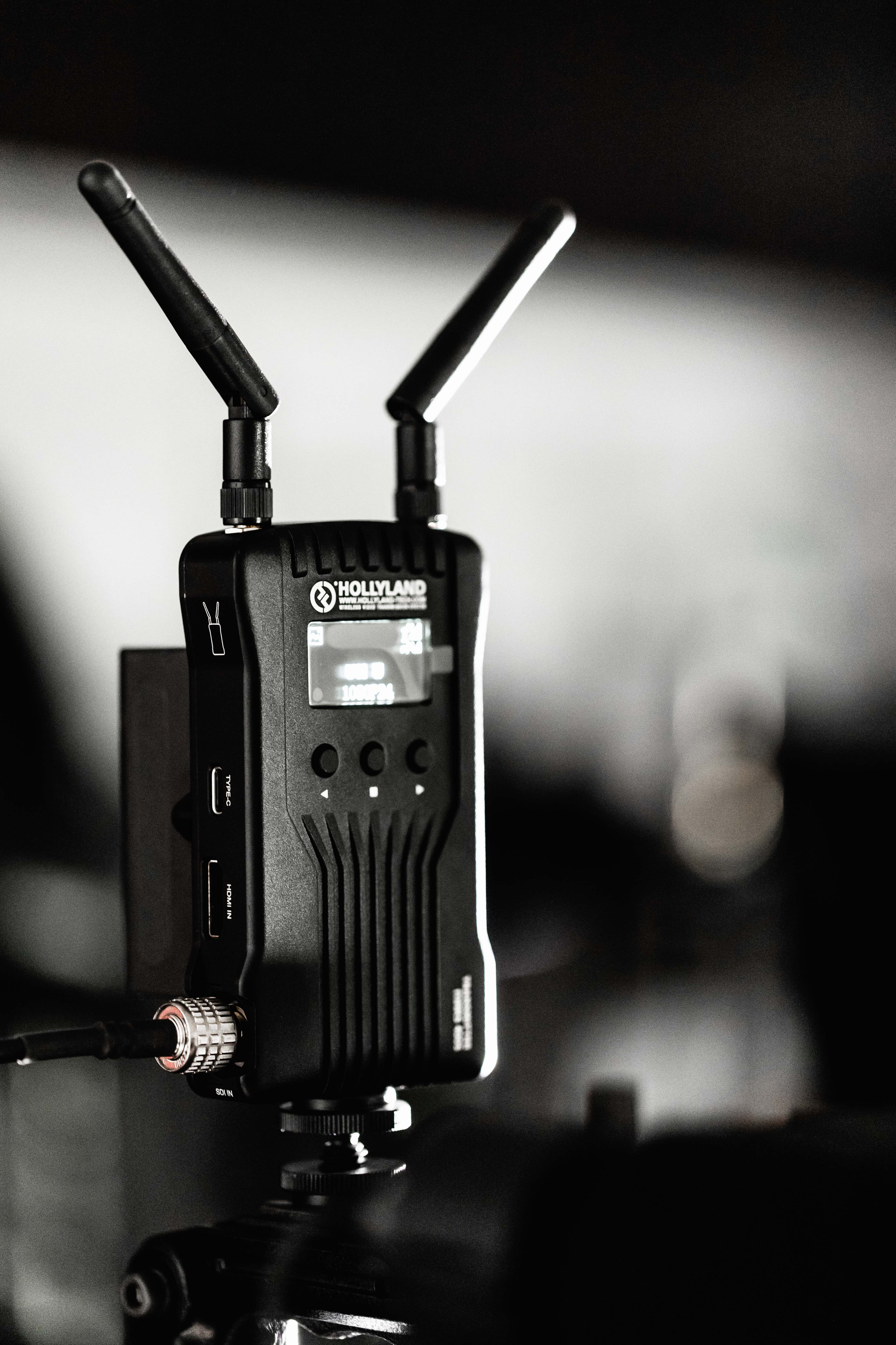 Image of close-up shot of a hollyland wireless transmitter with dual antennas, designed for video transmission. the device features connectors and a digital display, indicating its advanced technology. lighting highlights its sleek and professional build, making it ideal for videography and broadcasting setups.