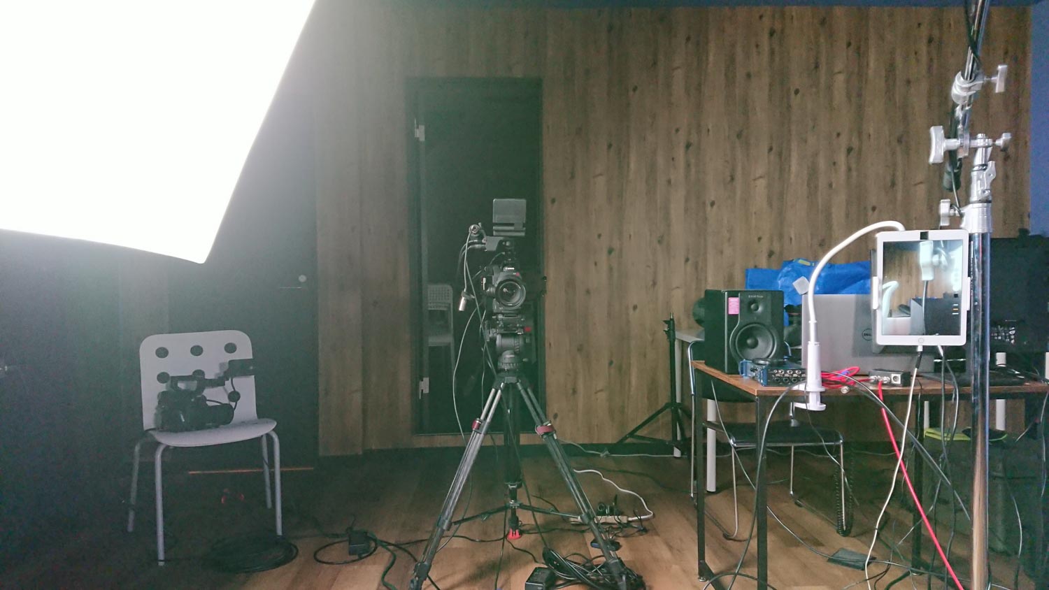 Image of a professional film production studio setup featuring a camera on a tripod, a large softbox light, and multiple audio-visual equipment on a desk. the wooden wall background, along with cables and sound equipment, creates an authentic video production environment. perfect seo