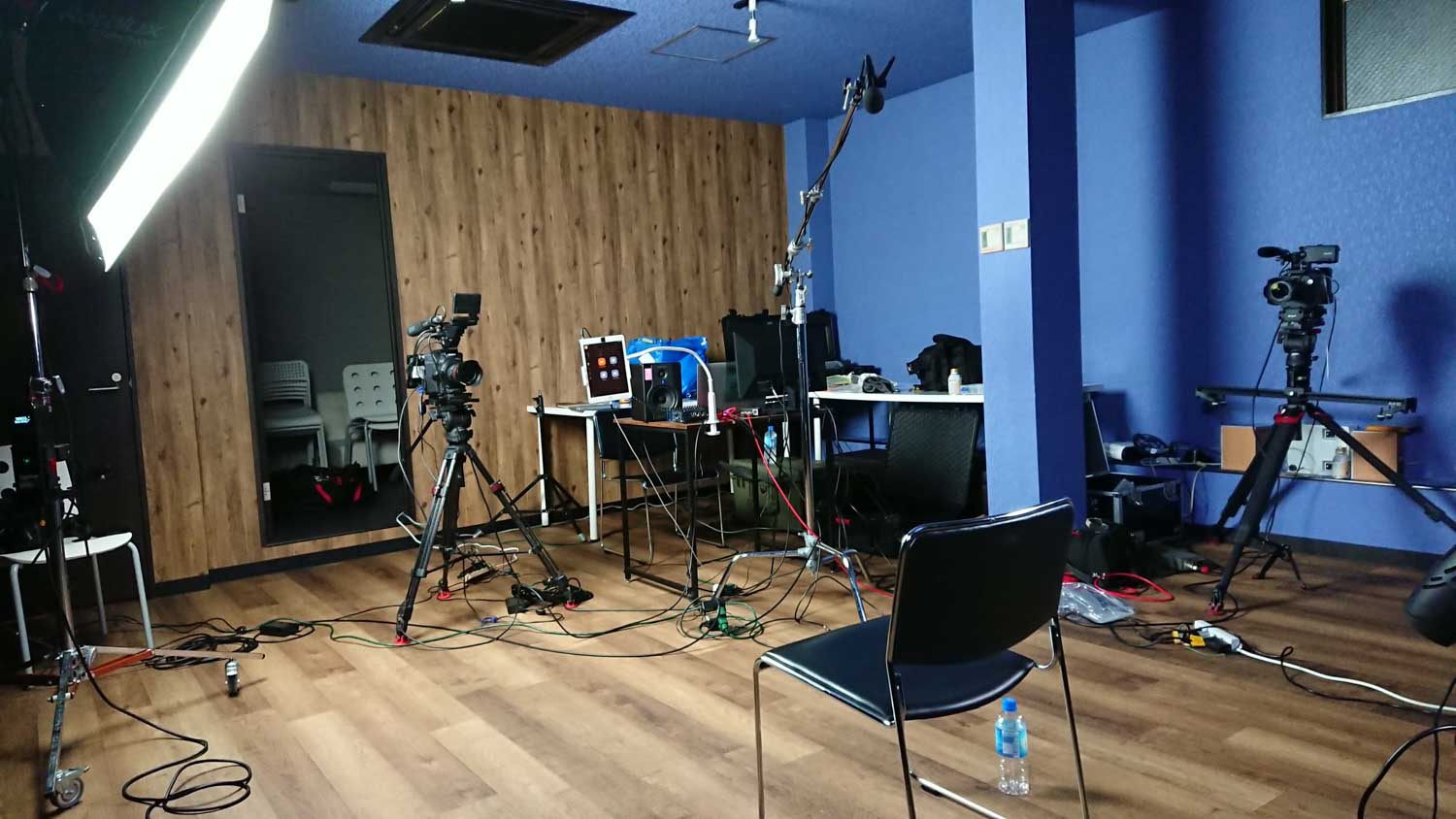 Image of this image showcases a professional video production studio setup, featuring cameras on tripods, lighting equipment, and sound gear. the studio has a blue and wood-themed interior with a hardwood floor. a desk is equipped with a laptop and various recording devices, highlighting
