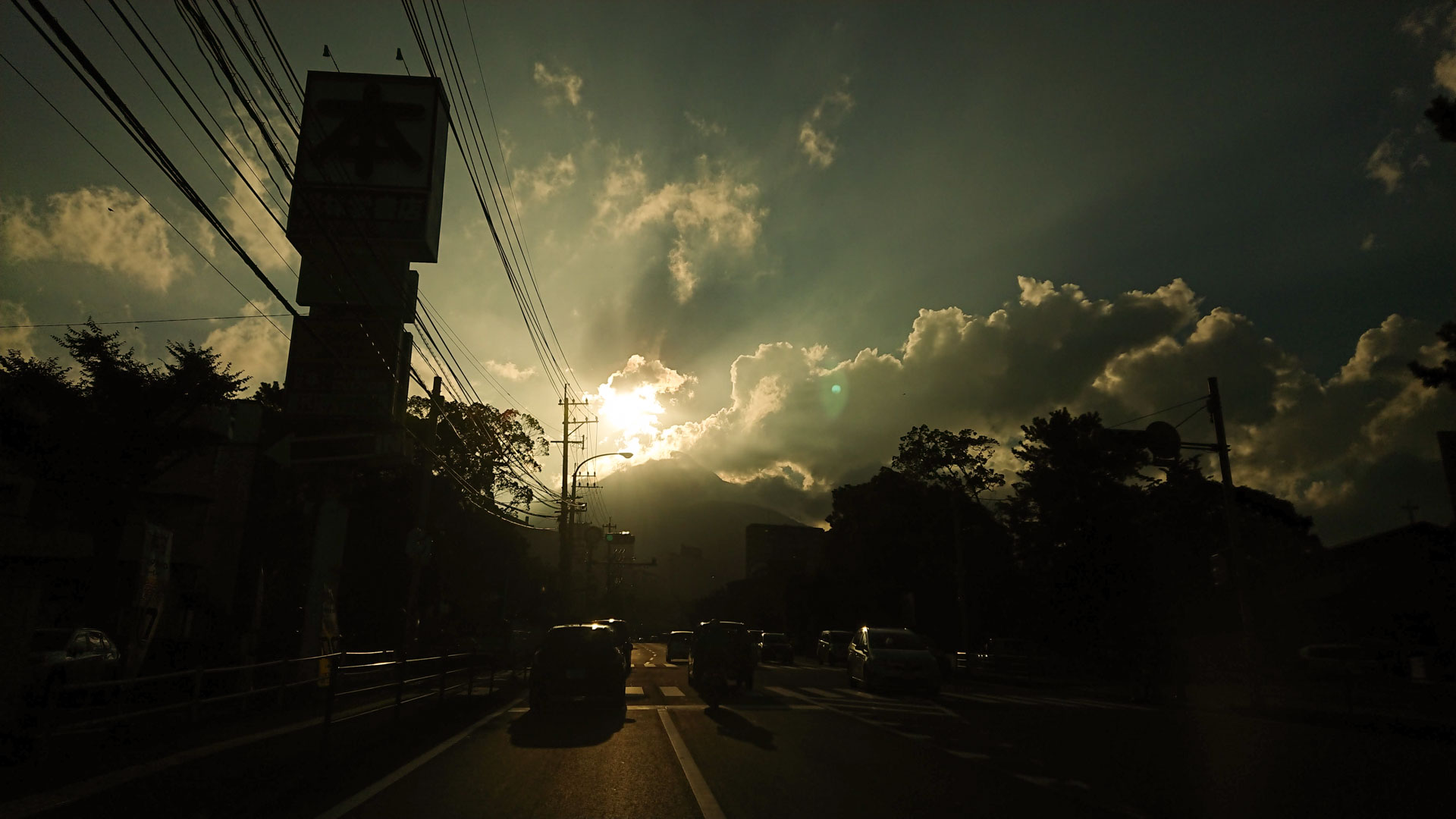 Image of dramatic sunset over a busy street in kagoshima, japan, with cars silhouetted against the glowing sky. the image captures an urban scene with telephone poles and wires intersecting the vibrant, cloudy horizon. ideal keywords: sunset, kagosh