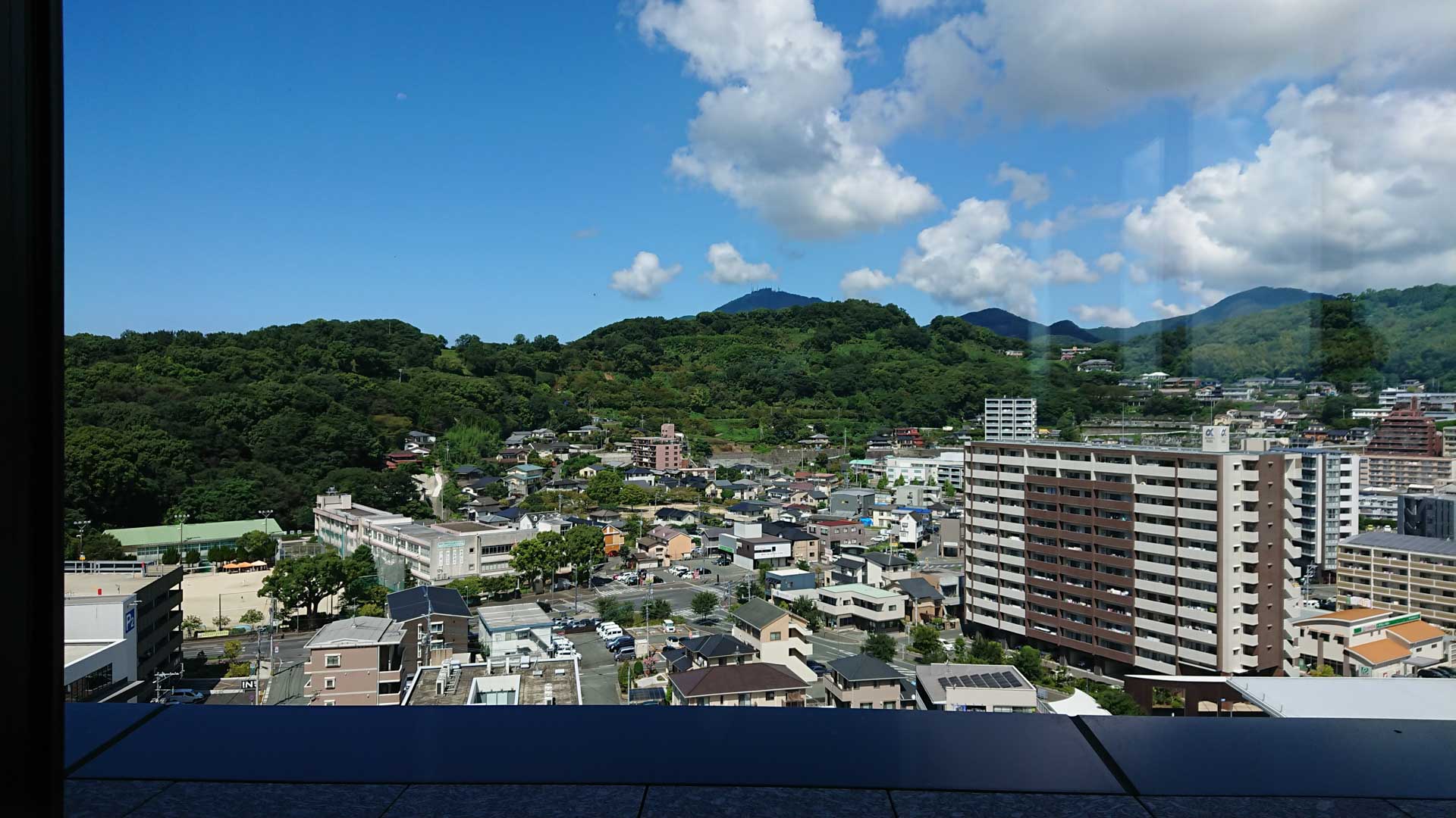 Image of panoramic view of a tranquil japanese cityscape featuring a blend of modern apartments and traditional houses, set against lush green hills under a vibrant blue sky. this serene urban scene captures the harmonious integration of nature and architecture, ideal for showcasing japanese landscape and