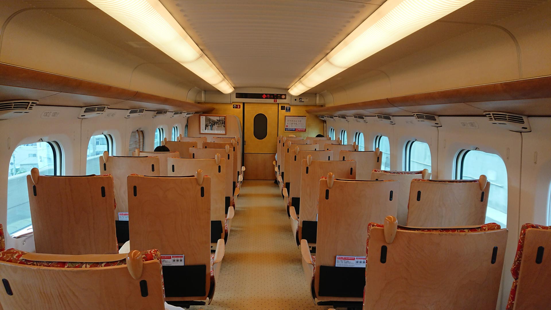 Image of this image showcases the interior of a modern japanese bullet train (shinkansen), featuring sleek wooden seats and large windows that allow ample natural light. the clean and spacious design exemplifies the efficiency and comfort associated with high-speed rail travel in japan. perfect