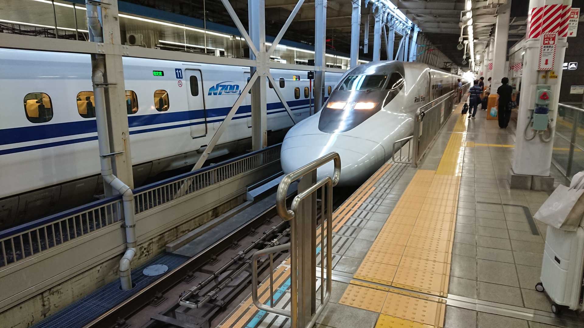 Image of a sleek shinkansen bullet train is stationed at a bustling platform in a japanese train station. the cutting-edge n700 series is known for its speed and efficiency, embodying modern rail travel. the platform is busy with passengers, capturing the essence of