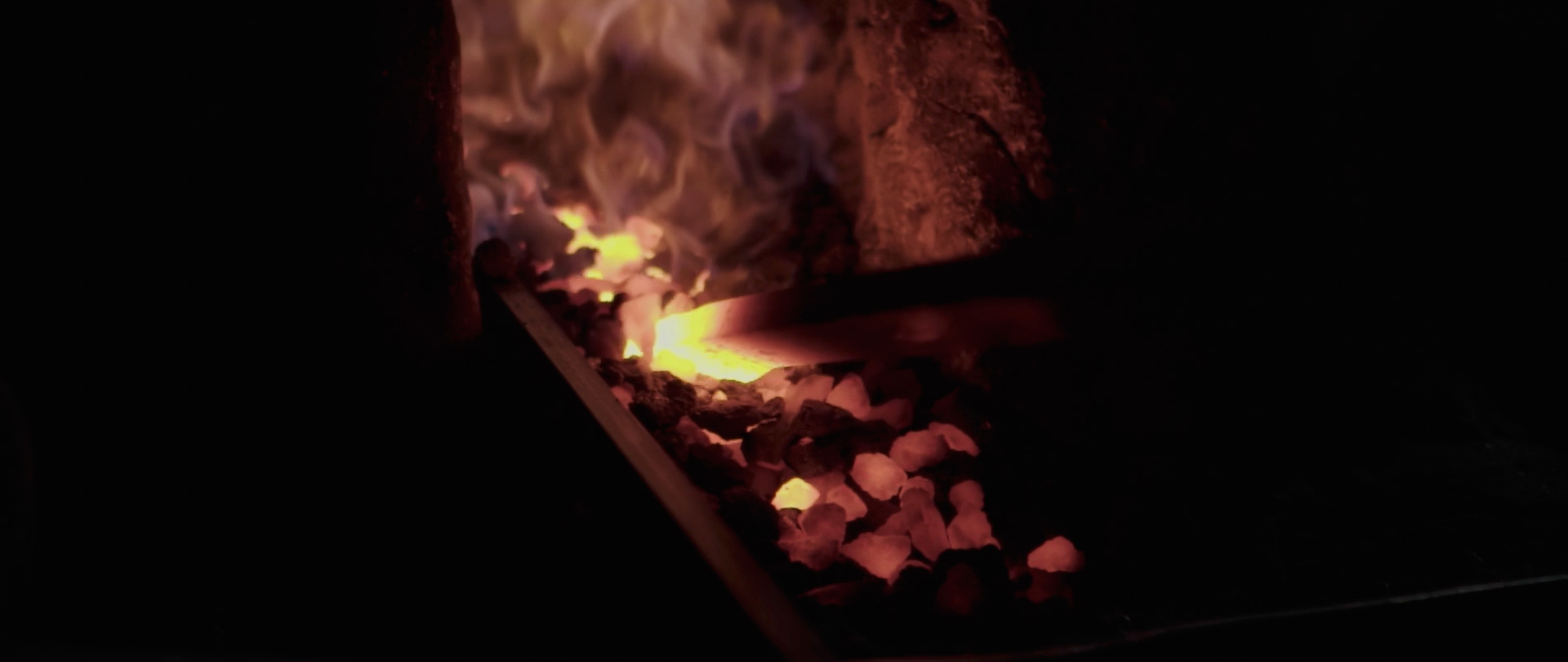 Image of this image captures a traditional blacksmith's forge, showcasing glowing coals and intense flames. the scene highlights a metalwork process, making it ideal for keywords like blacksmithing, metal forging, and traditional craftsmanship. the dark ambiance emphasizes the fiery heat