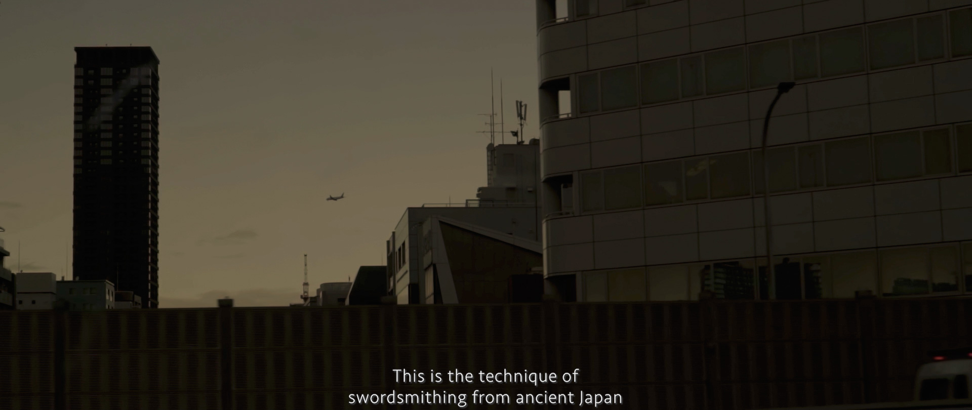 Image of the image depicts a cityscape at dusk, highlighting silhouetted modern buildings against a dimly lit sky. a small airplane is visible in the distance, contributing to the urban atmosphere. the foreground features text mentioning japanese swordsmithing, suggesting a cultural or