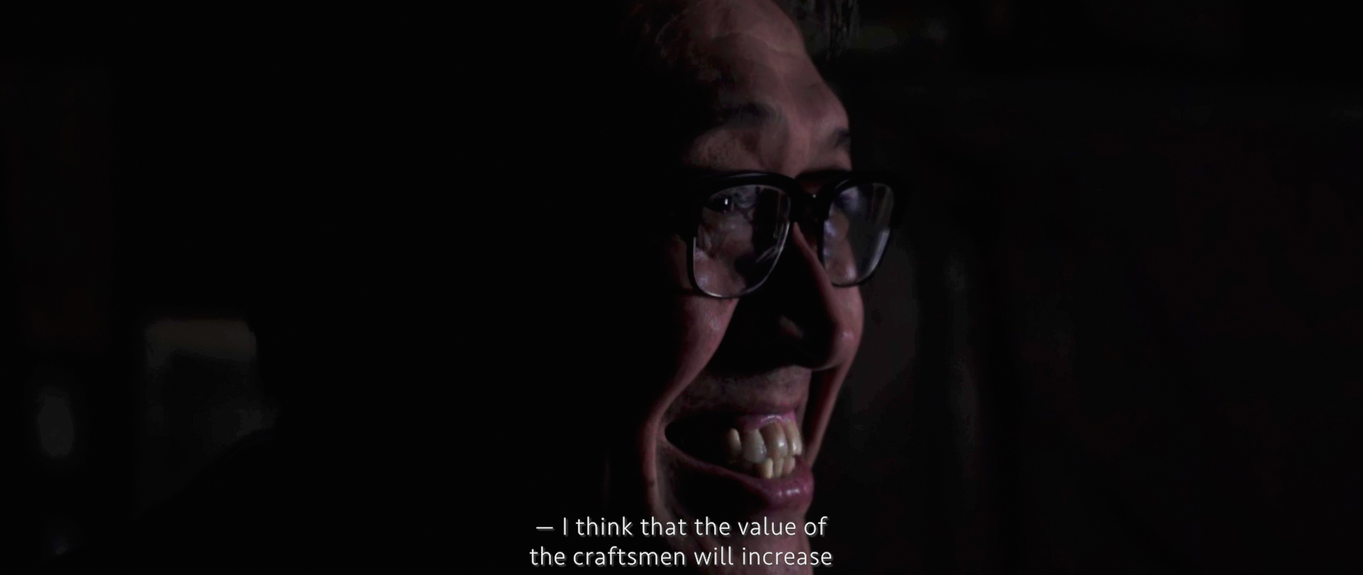 Image of a close-up image of a person speaking in a dimly lit setting, featuring a thoughtful expression and wearing glasses. the subtitles read, "i think that the value of the craftsmen will increase," highlighting a discussion about artisan skills and craftsmanship value. ideal