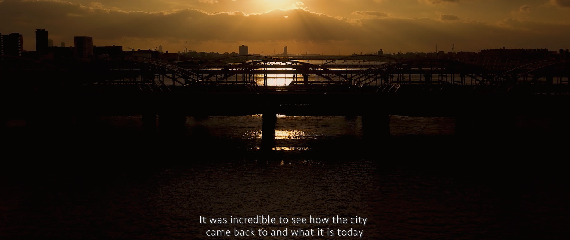 Image of sunset over a city skyline with a silhouetted bridge and river in the foreground. the golden hues reflect beautifully on the water, creating a serene urban landscape. this captivating scene illustrates the peaceful transformation of the city at dusk. perfect as a representation of