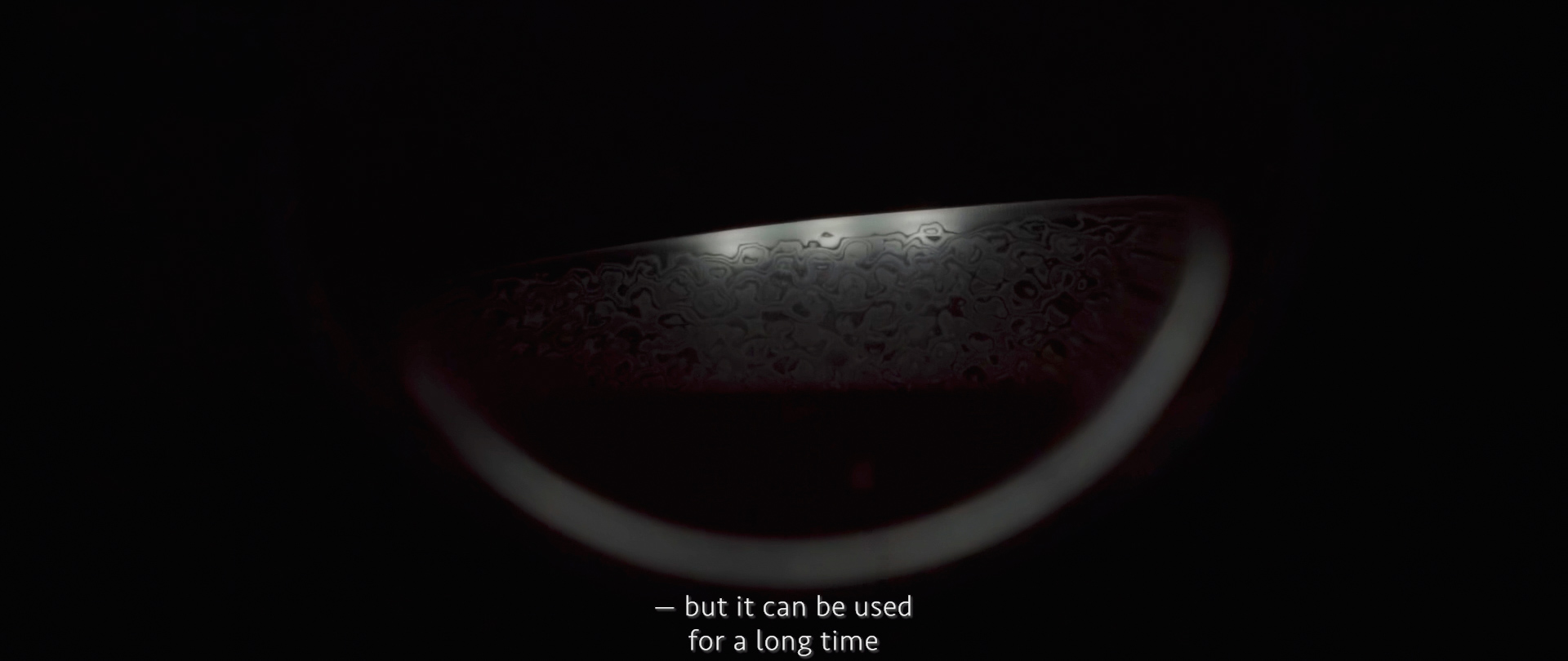 Image of the image captures a close-up of a damascus steel pattern on a knife blade, highlighting its intricate and wavy design. the dark background emphasizes the steel's texture and craftsmanship. subtitles at the bottom mention its durability, reading “— but it