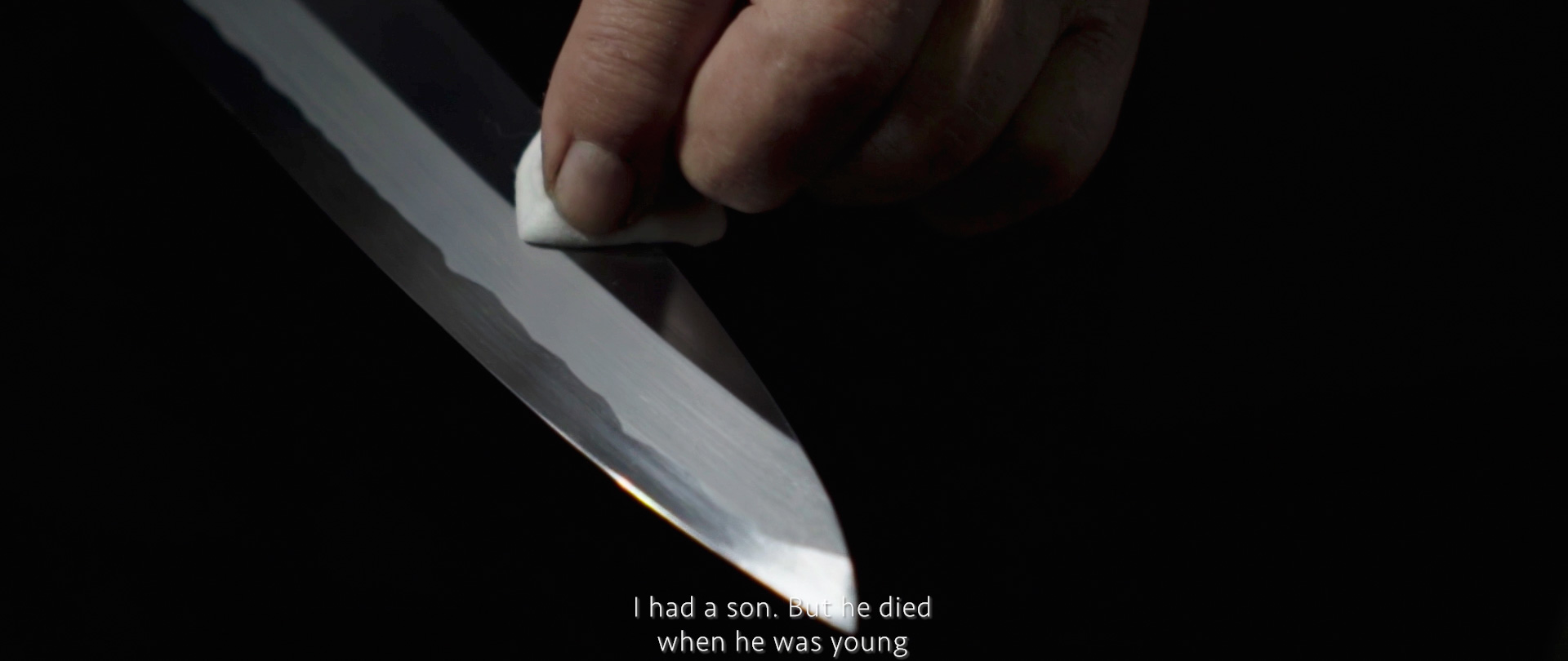 Image of a close-up image of a hand meticulously polishing a japanese katana sword, highlighting the blade's sharpness and craftsmanship. the setting is dark, emphasizing the gleam on the metal. there's text overlay expressing a somber personal story. keywords: kat