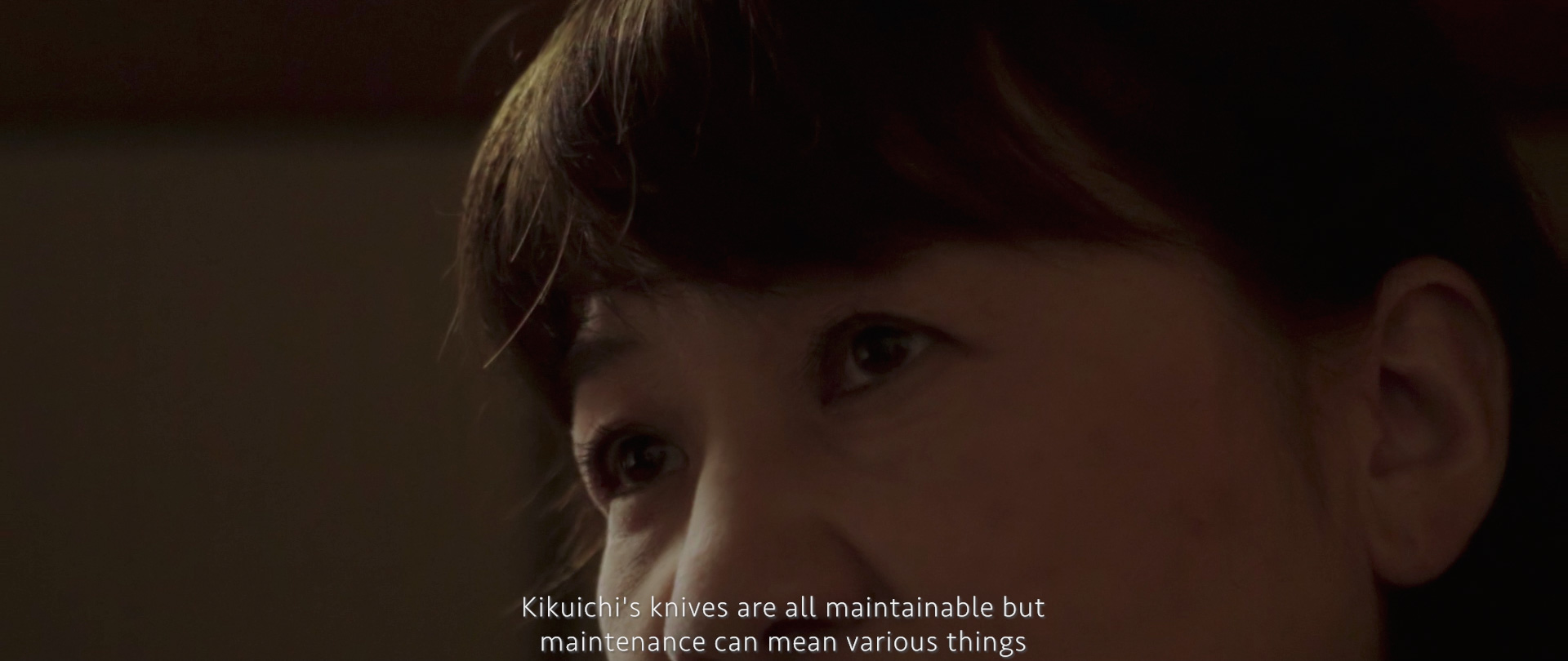 Image of close-up of a person's eyes with a thoughtful expression in a dimly lit setting. subtitles provide context about the maintenance of kikuchi's knives. keywords: close-up, thoughtful, kikuchi knives, maintenance, dimly lit.