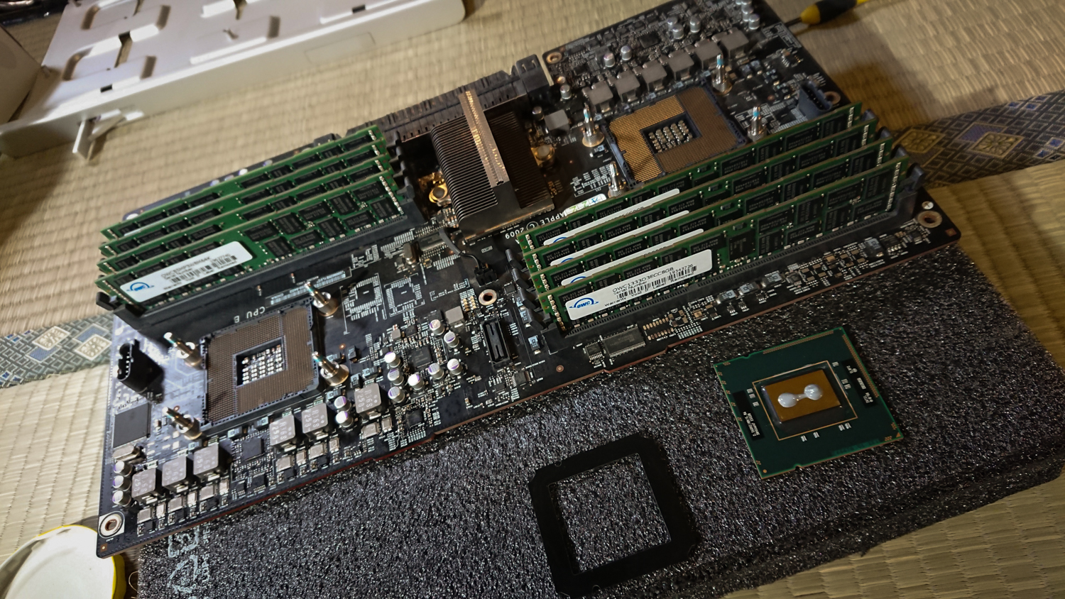 Image of image of a computer motherboard with multiple ram modules installed, set on a table. nearby, a detached processor lies beside the board, indicating a hardware upgrade or repair. perfect for keywords like "computer hardware," "motherboard," "ram upgrade," and