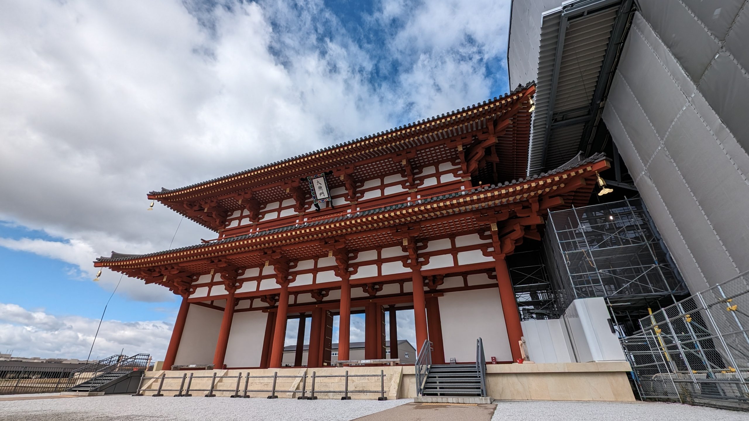 Image of ancient japanese architecture in nara: daigokuden hall at heijo palace. traditional red wooden pillars and intricate roof design under a partly cloudy sky. historic site undergoing renovation, reflecting japan's rich cultural heritage.